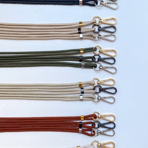 K&ouml;nnte beinhalten: F&uuml;nf S&auml;tze von Lanyards mit goldenen und schwarzen Akzenten. Jedes Lanyard hat zwei schwarze Metallverschl&uuml;sse und einen goldenen Ring. Die Lanyards sind in den Farben Schwarz, Beige, Gr&uuml;n, Braun und Wei&szlig;.