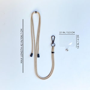 K&ouml;nnte beinhalten: Ein beiger Lanyard mit schwarzen Endkappen und einem durchsichtigen Plastik-Badgehalter. Das Lanyard ist 106,7 cm lang und der Badgehalter ist 5,3 cm breit und 4 cm hoch.