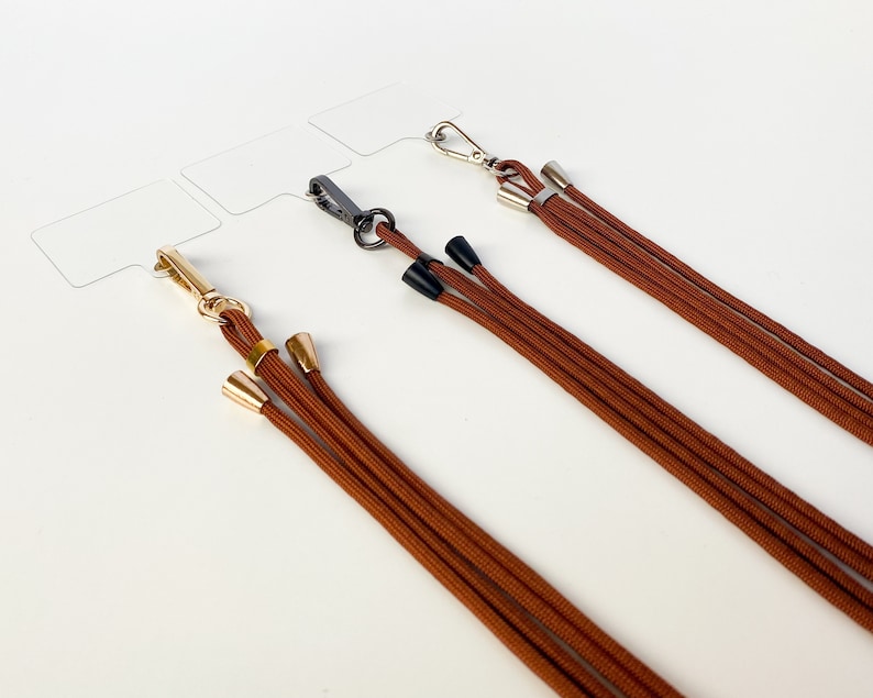 K&ouml;nnte beinhalten: Drei braune Kordel-Lanyards mit goldenen und silbernen Verschl&uuml;ssen und schwarzen und goldenen Endkappen.