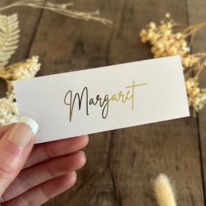 May include: White place card with the name "Margaret" written in gold foil lettering.