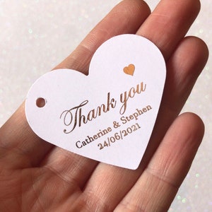 Può includere: Etichetta di ringraziamento a forma di cuore bianca con scritta in oro. L'etichetta dice "Grazie Catherine & Stephen 24/06/2021".