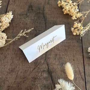May include: White place card with a gold inscription that reads "Margaret".
