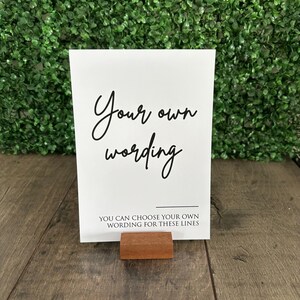 May include: White card with black text that reads "Your own wording" and "You can choose your own wording for these lines". The card is standing on a small wooden easel.