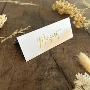 May include: White place card with a gold inscription that reads "Margaret".