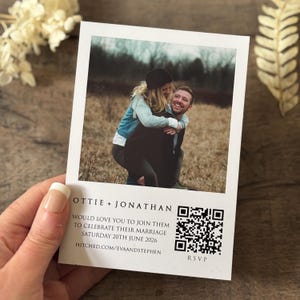 May include: A wedding invitation featuring a photograph of a couple in a field. The invitation includes the couple's names, the wedding date, and a QR code for RSVP.