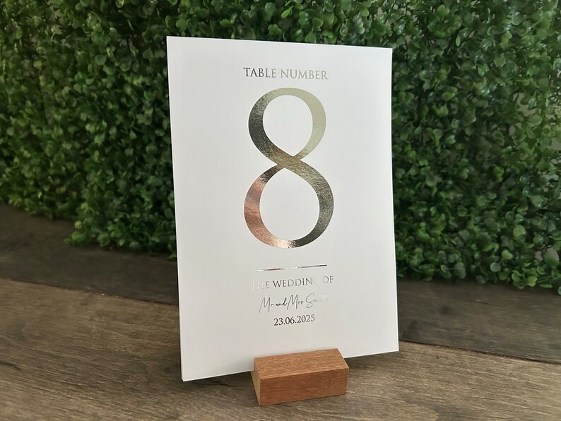 May include: White table number card with a silver foil number 8. The card has the text "Table Number" and "The Wedding of Mr. & Mrs. Smith 23.06.2025".