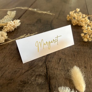 May include: White place card with the name "Margaret" written in gold script.