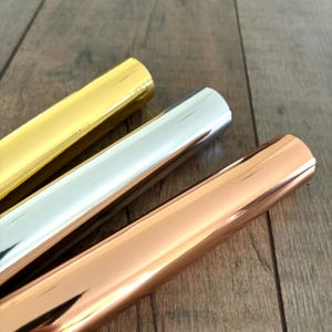 May include: Three rolls of metallic wrapping paper in gold, silver, and rose gold.