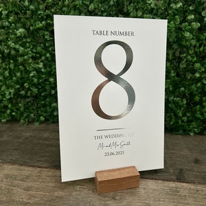 May include: Silver table number card with the number 8 printed in a large font. The card also includes the text "TABLE NUMBER" and "THE WEDDING OF Mr. and Mrs. Smith 23.06.2025".