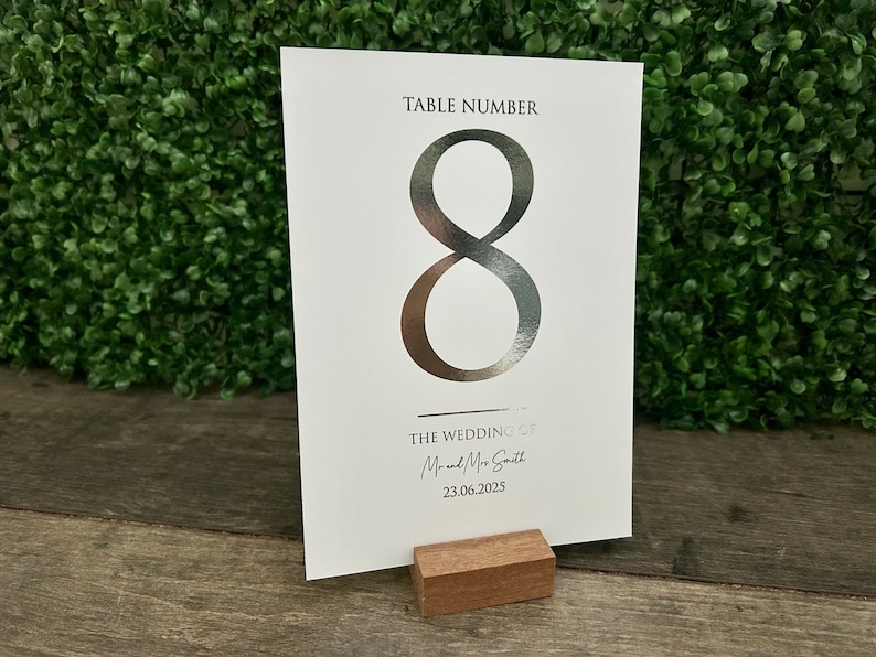 May include: Silver table number card with the number 8 printed in a large font. The card also includes the text "TABLE NUMBER" and "THE WEDDING OF Mr. and Mrs. Smith 23.06.2025".