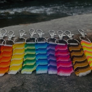 May include: A set of ten colourful keychains with a chevron pattern. Each keychain is made of woven yarn and has a silver metal clasp.