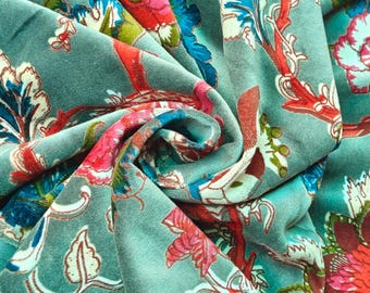 May include: Close-up of a teal fabric with a floral pattern. The design features large flowers in shades of red, pink, and blue, with white and green accents. The fabric is folded, showing the texture and depth of the material.