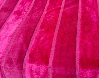 May include: Close-up of a vibrant fuchsia fabric with vertical stripes. The fabric has a plush, velvety texture, with the stripes appearing as slightly raised bands. The color is a rich, saturated pink, creating a bold and eye-catching visual.