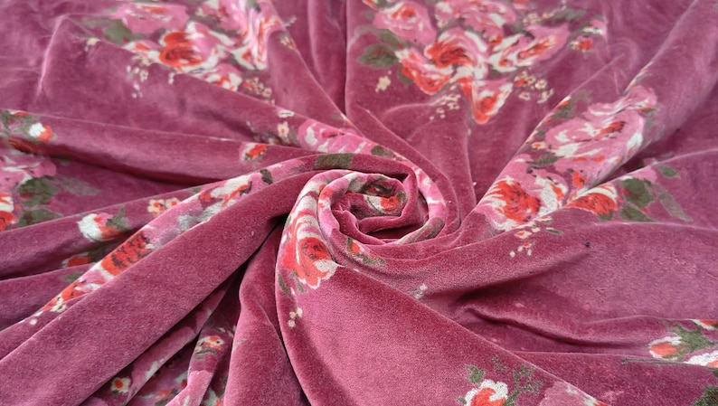 May include: Pink velvet fabric with a floral pattern. The fabric is soft and luxurious, and the floral pattern is delicate and feminine.