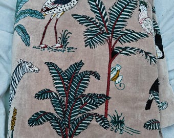 May include: A beige fabric with a tropical print featuring flamingos, zebras, palm trees, and birds. The fabric has a soft, velvety texture.