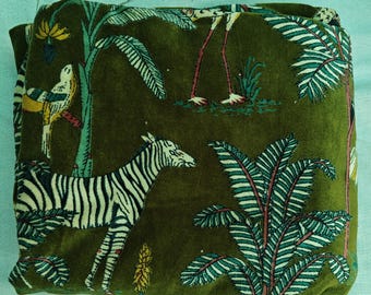 May include: Olive green fabric with a repeating pattern of zebras, birds, and stylized trees. The design features black and white zebras, yellow and white birds, and palm trees with teal and red accents. The fabric is folded.