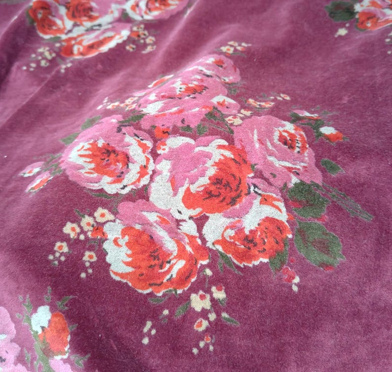 May include: A close-up of a burgundy fabric with a floral pattern of pink and red roses. The fabric has a soft, velvety texture.