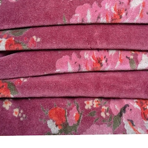 May include: Close-up of a folded fabric with a pink floral pattern. The fabric has a soft, velvety texture.