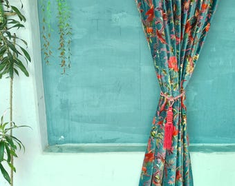 May include: A teal velvet curtain with a vibrant floral pattern in red, orange, and green. The curtain is tied with a pink tassel. The background is a teal wall with a hanging plant.