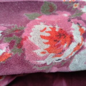 May include: Close-up of a pink and white floral fabric with a textured, fuzzy surface. The fabric features a large pink and white flower with red accents.