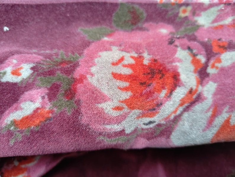 May include: Close-up of a pink and white floral fabric with a textured, fuzzy surface. The fabric features a large pink and white flower with red accents.