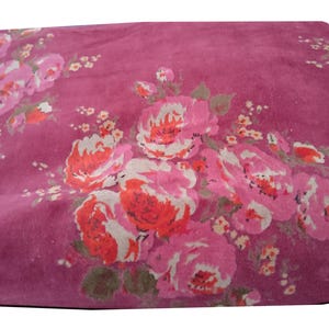 May include: A pink fabric with a floral pattern featuring pink, red, and white flowers. The fabric has a soft, velvety texture.