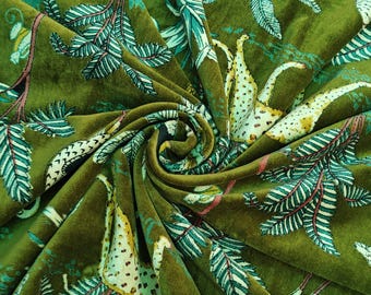 May include: Close-up of olive green velvet fabric with a jungle-themed pattern. The design features stylized leopards, palm fronds, and other tropical foliage in shades of white, yellow, and teal. The fabric is folded, creating shadows and depth.