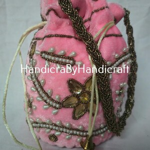 Könnte beinhalten: Rosa Samt-Kordelzugbeutel mit Perlenbesatz und floralem Design. Die Tasche hat einen geflochtenen Riemen und dekorative Quasten. Der Text "HandicraByHandicraft" ist sichtbar.