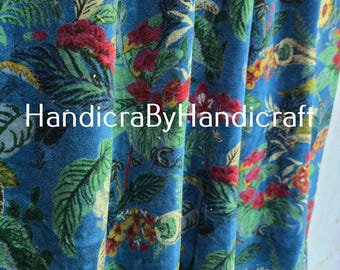 May include: Blue fabric with a floral pattern featuring red, yellow, and green flowers and leaves. The fabric has the text "HandicraByHandicraft" in white. The fabric is likely used for curtains or upholstery.