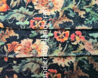 May include: Close-up of a fabric with a dark blue background and a floral pattern. The flowers are in shades of orange, red, and cream, with green leaves. The fabric is folded, showing multiple layers.