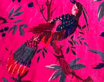 May include: A vibrant pink fabric featuring a detailed bird and floral pattern. The bird has a mix of blue, red, and brown feathers, perched on a branch with green leaves. The background is a solid, bright pink.