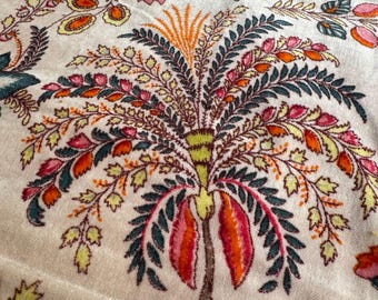 May include: Close-up of a cream-colored fabric with a detailed floral pattern. The design features stylized trees and flowers in shades of orange, pink, green, and yellow. The fabric has a soft, velvety texture, suggesting a decorative textile.