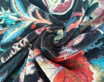 May include: Close-up of a dark teal fabric with a floral pattern. The design features large, stylized flowers in shades of red, blue, and teal, set against a dark background. The fabric is folded, showing the texture and depth of the material.