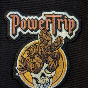Könnte beinhalten: Ein gestickter Aufnäher mit den Worten "Power Trip" in gotischer Schrift, mit einem Schädel, der eine Krone aus Kakteen trägt.