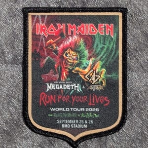 Peut inclure: Un écusson rectangulaire à bordure noire. Il affiche le texte "IRON MAIDEN" en rouge, ainsi que "MEGADETH & ANTRAX" et "RUN FOR YOUR LIVES WORLD TOUR 2026". L'écusson comprend également le texte "SEPTEMBRE 25 & 26 BMO STADIUM".