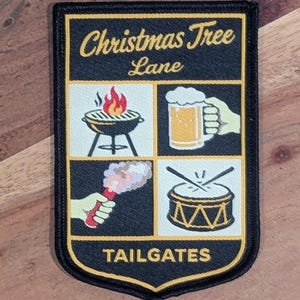 May include: Black and gold patch with the words "Christmas Tree Lane" and "Tailgates." The patch features illustrations of a grill with flames, a beer mug, a flare, and a drum. The patch has a black border.