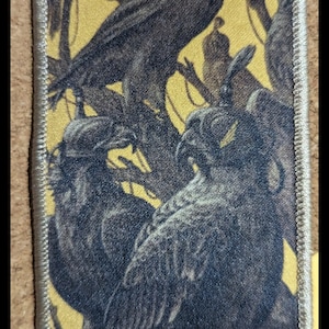 May include: A black and white embroidered patch with a design of crows perched on branches against a yellow background. The patch has a white border.