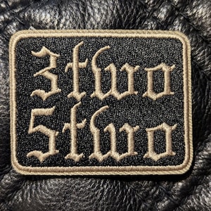 May include: A black embroidered patch with the word "Sfw" in white, old English lettering.