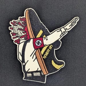 May include: Embroidered patch featuring a cartoon figure dabbing, with a shoe and a red and white design on the head. The figure wears a white shirt with suspenders and a Nazi symbol on the arm. The shoe has the text "LOS ANGELES".