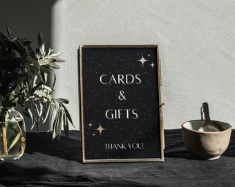 May include: A gold-framed sign with a black background and white text that reads "Cards & Gifts Thank You!" The background is decorated with gold stars.