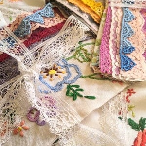 May include: A collection of fabric pieces with lace and embroidery. The fabrics are in shades of white, blue, yellow, pink, and red. Some have floral embroidery, while others feature delicate lace trim. The image shows a variety of textures and patterns.