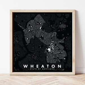 May include: A framed black and white map of Wheaton, Maryland, with the city name and state printed in white. The map features a detailed street layout and is encased in a light-colored wooden frame.