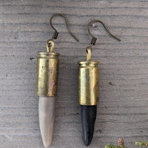May include: A pair of earrings made from brass bullet casings and wood. One earring has a light brown wood piece and the other has a dark brown wood piece.