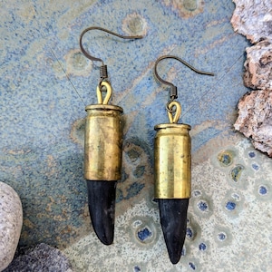 Puede incluir: Un par de pendientes hechos de casquillos de bala de latón y madera negra. Los pendientes tienen un diseño simple de gancho.