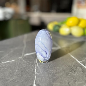 May include: A small, light blue glass vase with a white swirl pattern. The vase is sitting on a gray countertop.