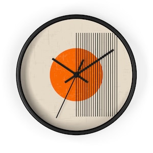 Puede incluir: Un reloj de pared redondo con marco negro y fondo beige. La esfera del reloj presenta un círculo naranja grande con líneas negras que irradian desde él. Las manecillas del reloj son negras.