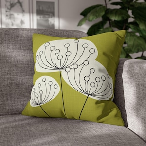 Puede incluir: Un cojín decorativo cuadrado con un fondo verde lima y un diseño floral blanco y negro. El cojín está colocado sobre un sofá gris, creando un aspecto moderno y elegante. El patrón floral añade un toque de elegancia inspirada en la naturaleza.