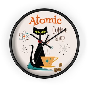 May include: A black and white clock with a black cat sitting on a teal blue surface. The cat is holding a yellow coffee cup. The clock face has the text "Atomic Coffee Shop" in orange and white. The clock has a black frame.