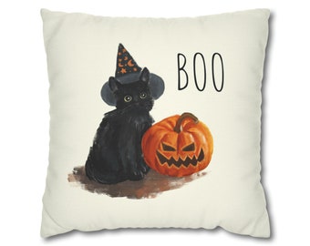May include: A square, off-white Halloween-themed pillow featuring a black cat wearing a witch hat with stars and moons. Beside the cat is an orange jack-o'-lantern. The word "BOO" is printed in black.