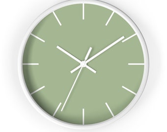 May include: A round wall clock with a white frame and a sage green face. White hands and hour markers provide a clean, minimalist design. The clock's face has a matte finish. The clock is a decorative item for home or office.